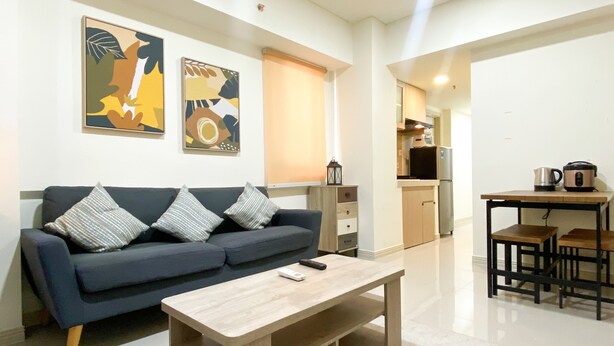 A modern living room with a sofa, coffee table, and artwork on the wall. - Best Spacious And Homey 2Br At Meikarta Apartment (Cikarang)