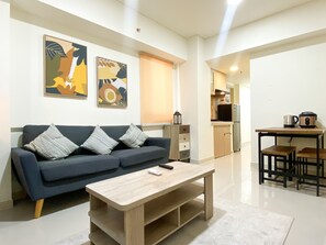 A modern living room with a sofa, coffee table, and artwork on the wall. - Best Spacious And Homey 2Br At Meikarta Apartment (Cikarang)