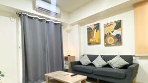 A living room with a dark grey sofa, a wooden coffee table, and a grey curtain. - Best Spacious And Homey 2Br At Meikarta Apartment (Cikarang)