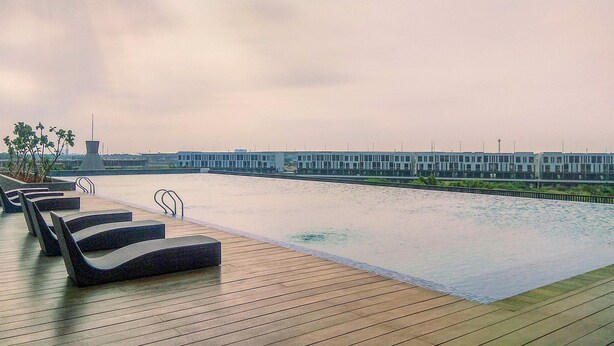 Une piscine à débordement située sur le toit, avec des chaises longues et une vue sur un bâtiment moderne de l’autre côté de l’eau.