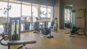 Une salle de sport équipée de divers appareils d’exercice, dotée de grandes fenêtres et offrant une vue sur des plantes extérieures.
