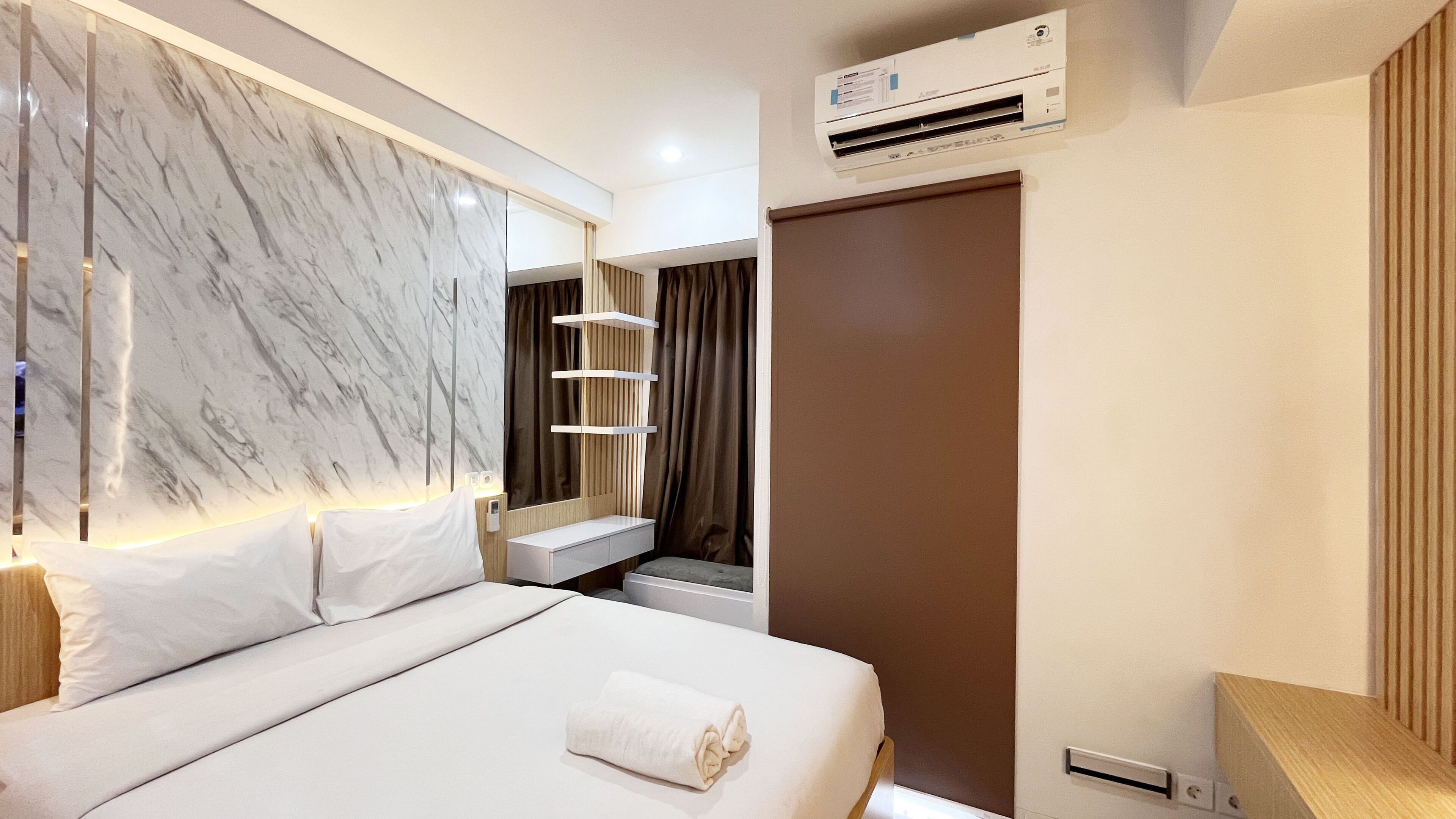 A modern hotel room with a marble headboard, a bed with white linens, a bedside table, a mirror, a built-in shelf, and an air conditioning unit.