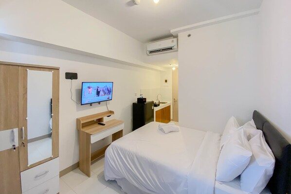 A hotel room with a bed, a desk, a TV, a wardrobe, and an air conditioning unit.