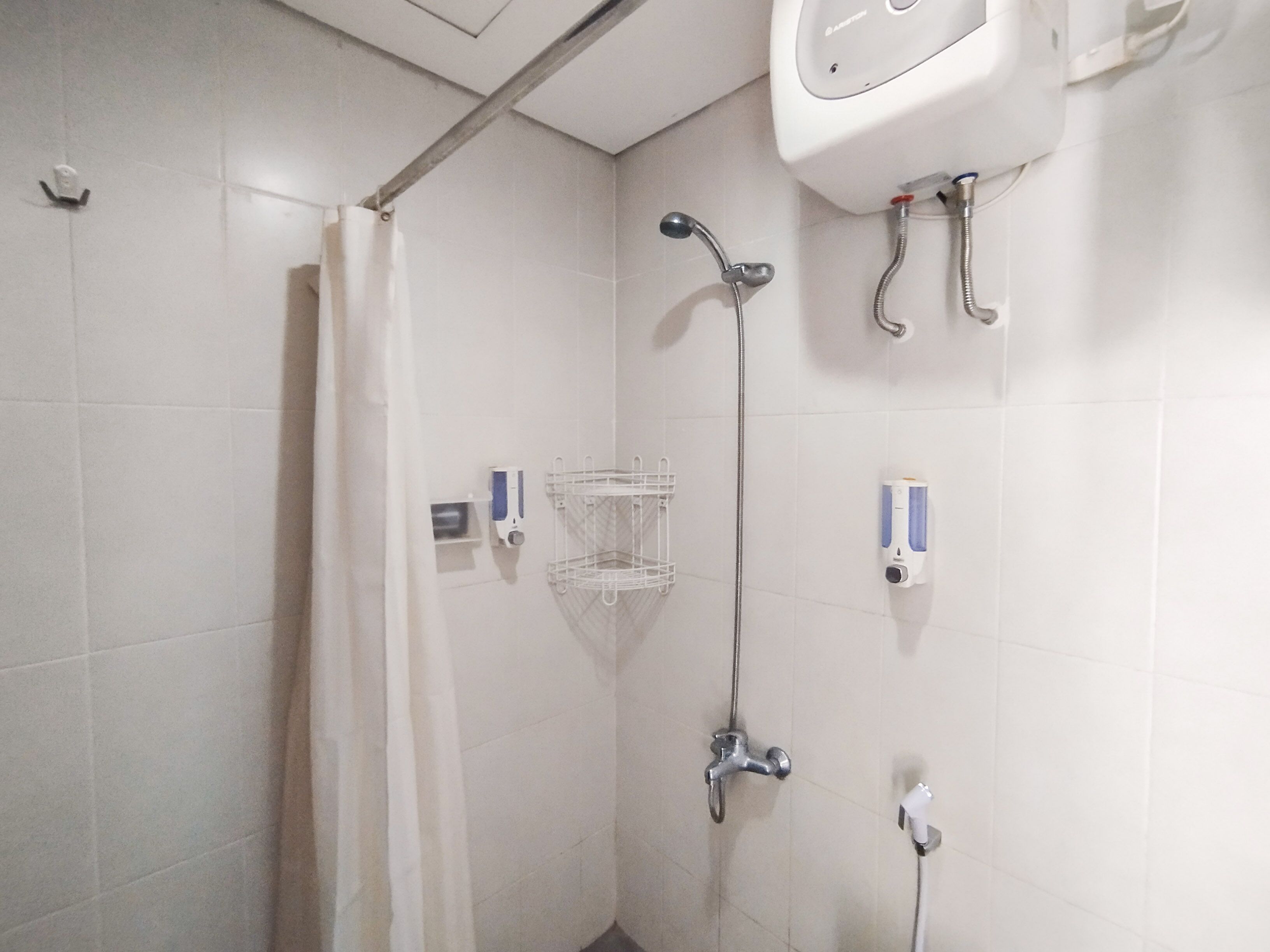 A shower area with a showerhead, a hand dryer, and a soap dispenser.