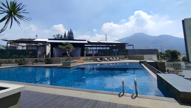A swimming pool with lounge chairs, a covered seating area, and a mountain view in the background. - Strategic And Comfy Studio At Skyland City Jatinangor Apartment (Hegarmanah)