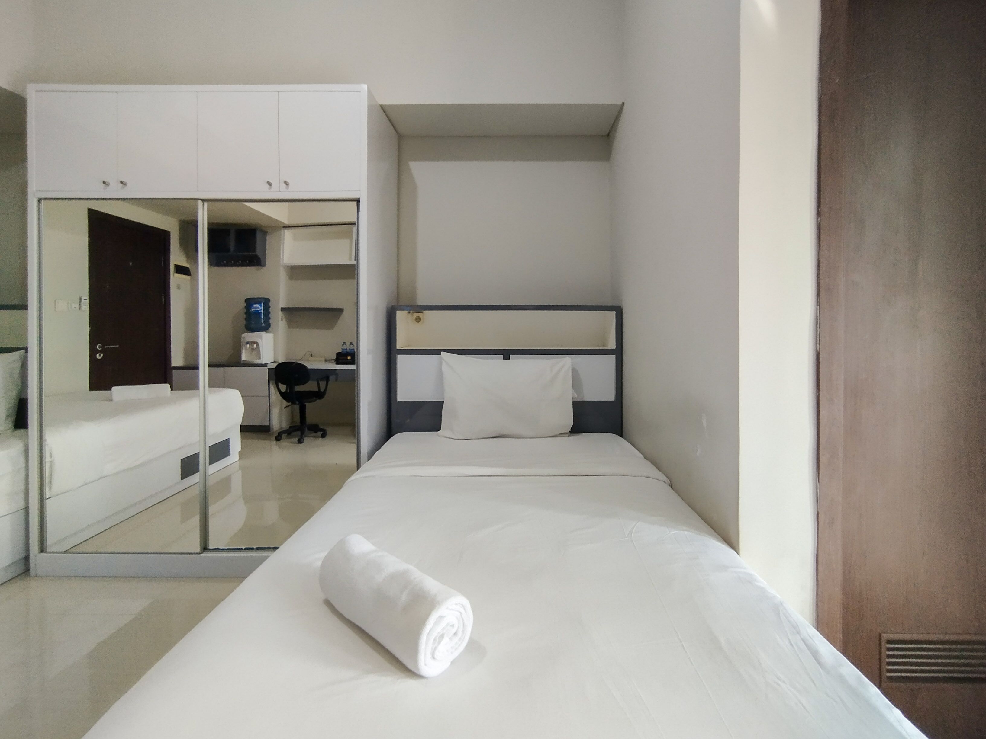 A hotel room with a bed, a desk, a chair, and a wardrobe.