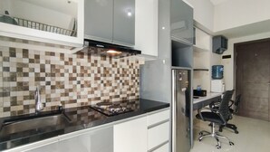 A modern kitchen with a checkered backsplash, stainless steel appliances, and a dining area with a water dispenser. - Strategic And Comfy Studio At Skyland City Jatinangor Apartment (Hegarmanah)