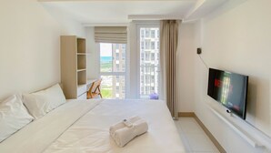 Une chambre d’hôtel avec un grand lit, une télévision et une vue sur les bâtiments et la verdure, visible par la fenêtre.