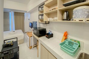 Una habitación de hotel compacta con cama, una kitchenette pequeña, televisión, dispensador de agua y microondas.