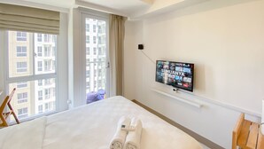 Une chambre d’hôtel avec un grand lit, un téléviseur fixé au mur et une vue sur la ville par la fenêtre.