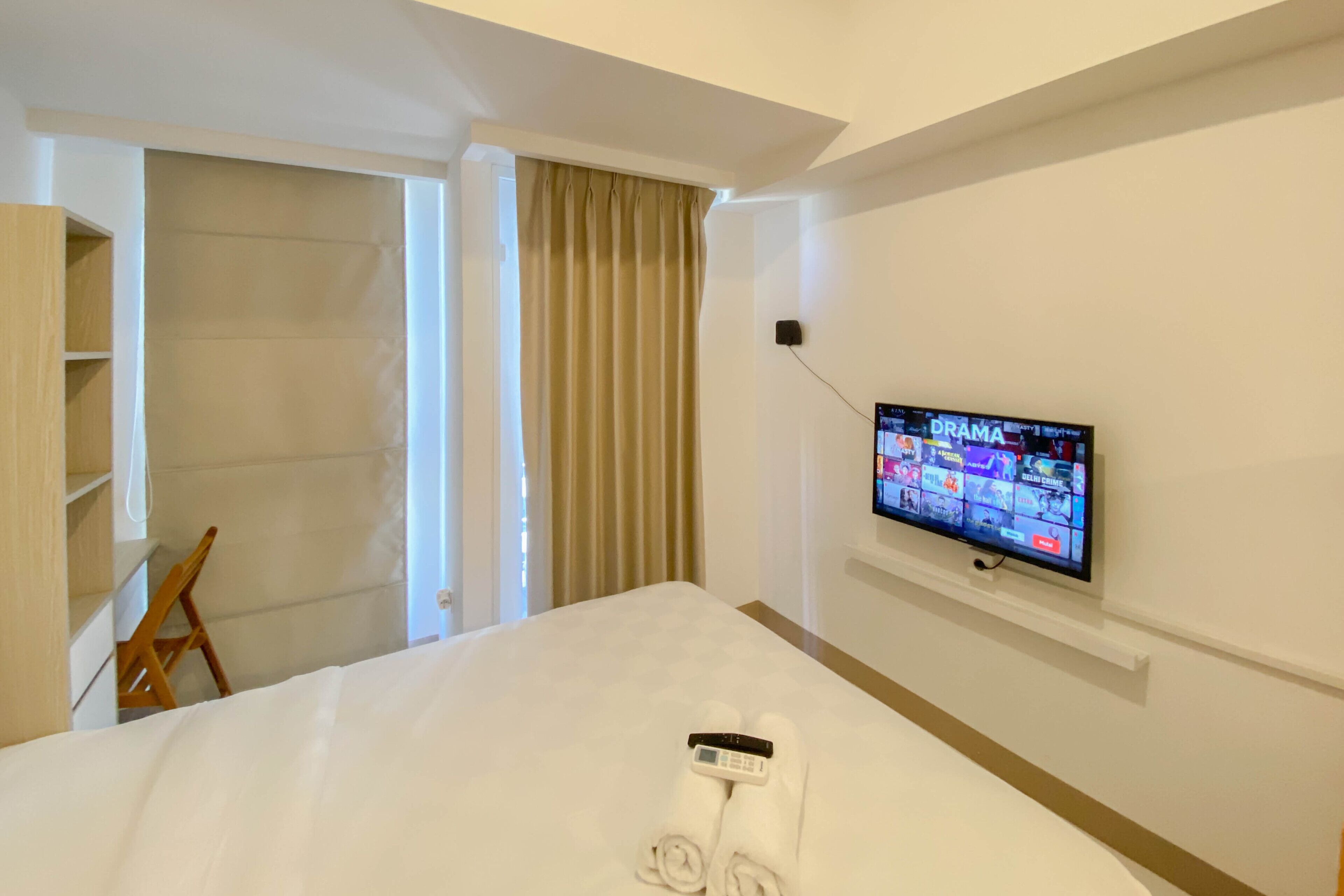 A hotel room with a bed, a TV mounted on the wall, a wooden chair, and a wardrobe.