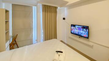 A hotel room with a bed, a TV mounted on the wall, a wooden chair, and a wardrobe.