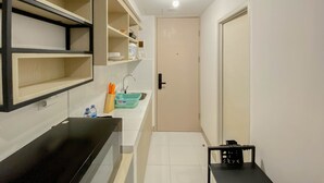 Une cuisine compacte avec des carreaux blancs, un plan de travail noir et un évier. Des étagères sont fixées au mur, et une porte est visible au fond.