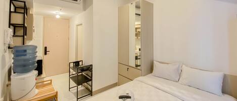 A hotel room with a bed, a bedside table with a water dispenser, a mirror, and a wardrobe.