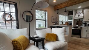 A modern living room with a sofa, a small table, and a kitchen in the background. - Black Brindle Cottage, Downtown Ft. Myers: Walk to Best Eats and Shops! (Fort Myers)