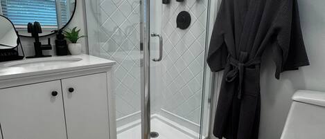 A modern bathroom with a glass-enclosed shower, white vanity, and a robe hanging on the wall.