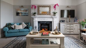 A living room with a fireplace, a sofa, a coffee table with books, and a TV.