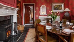 A dining room with a fireplace, a dining table set for four, and a red patterned wall.