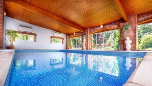 Una piscina interior con agua cristalina, vigas de madera en el techo y paredes de ladrillo.