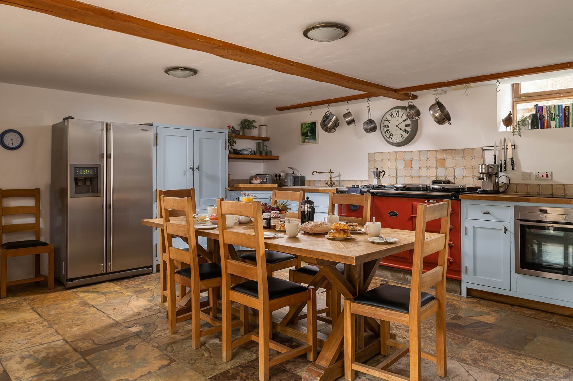 A kitchen with a dining table, chairs, a refrigerator, a stove, and various kitchen utensils.