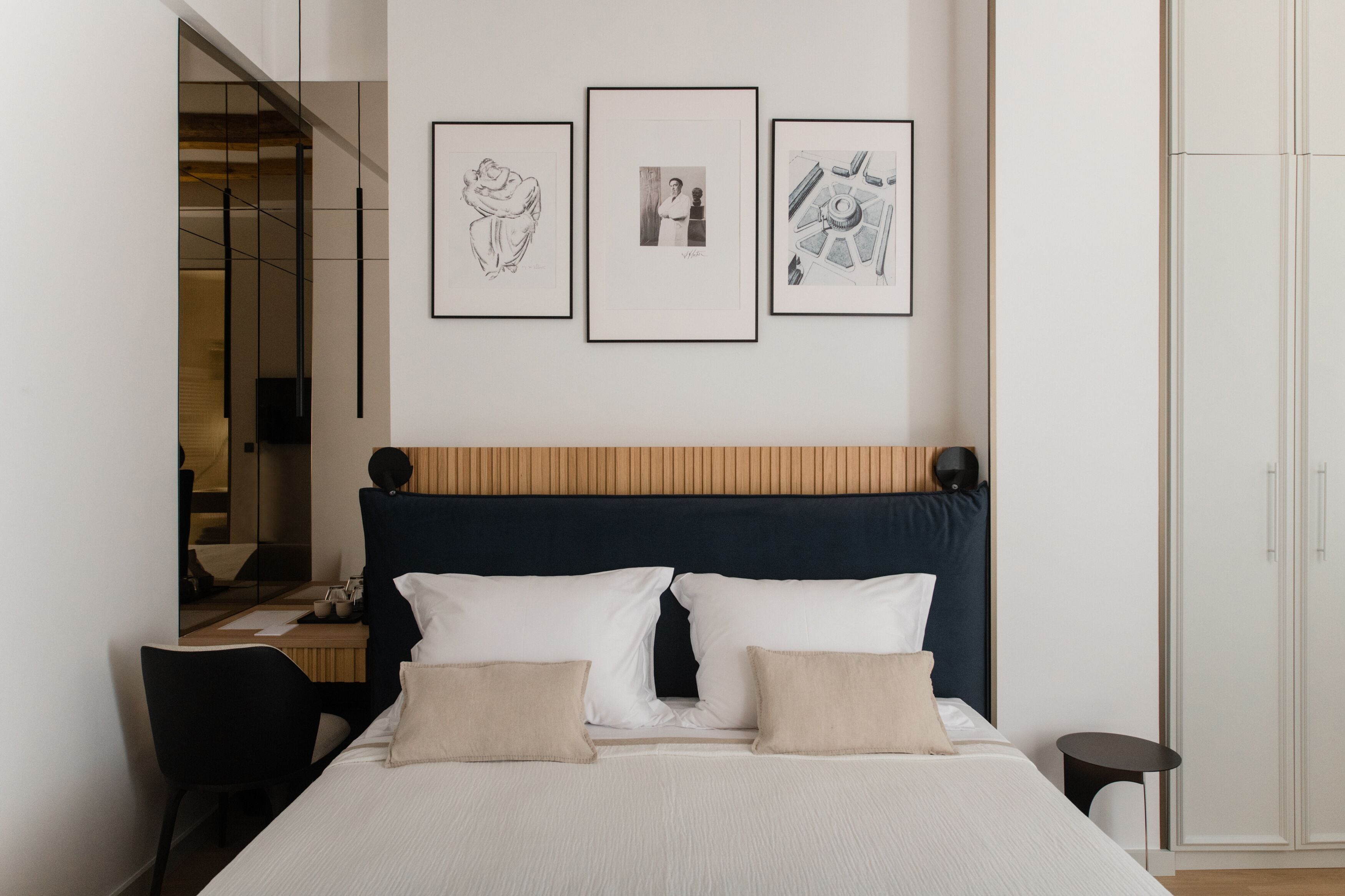 A neatly arranged hotel room with a bed, bedside table, chair, and a wall with three framed pictures.