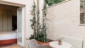 A bedroom with a bed, a glass door leading to a balcony, a wicker chair, a round table with a potted plant, and a brick wall. - Boutique HOH (Zagreb)