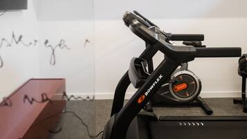 A treadmill in a room with a white wall and a mounted television.