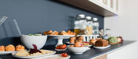 A buffet table with various food items and a white bowl with a spoon.