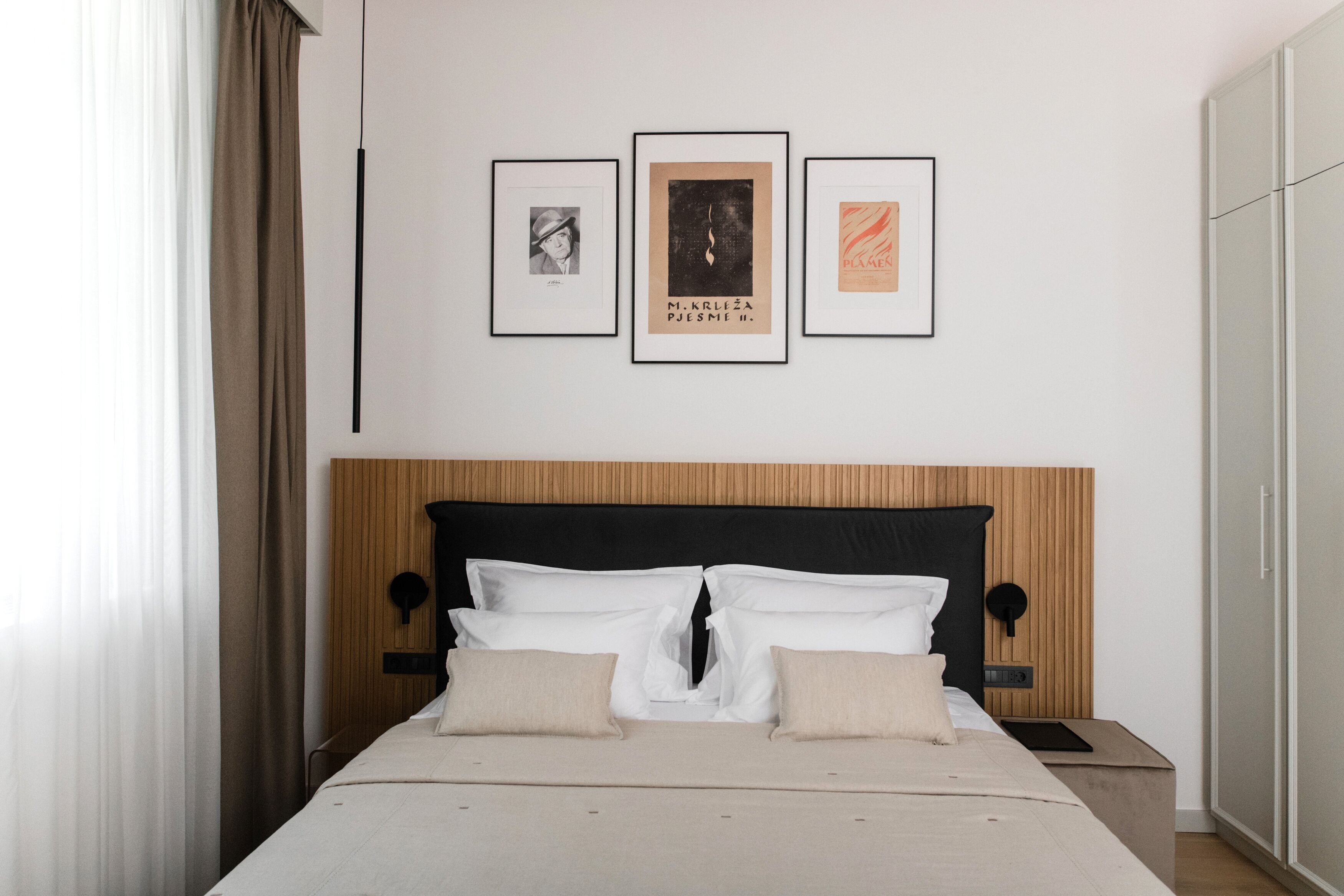 A neatly made bed with a wooden headboard, a bedside table, and three framed artworks on the wall.