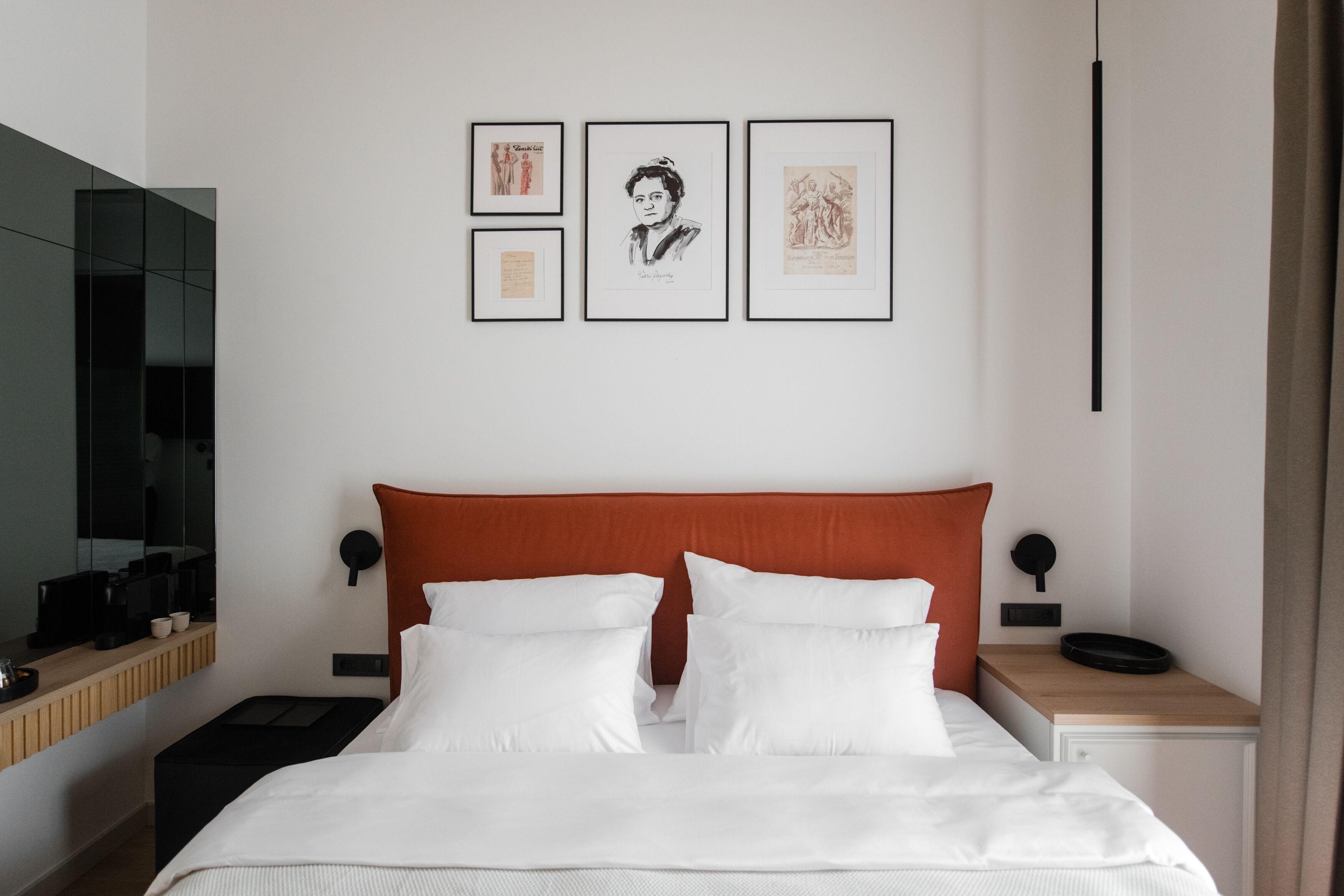 Una habitación de hotel moderna con una cama grande, una mesita de noche con lámpara, una mesita auxiliar y un televisor montado en la pared.