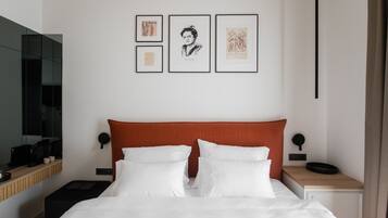 Una habitación de hotel moderna con una cama grande, una mesita de noche con lámpara, una mesita auxiliar y un televisor montado en la pared.