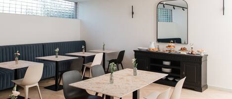 A modern dining area with tables, chairs, and a dark-colored buffet.