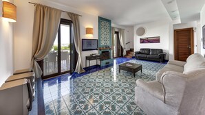 Un salon avec un canapé, une table basse et un téléviseur. Il y a une cheminée et une porte qui donne sur un balcon.