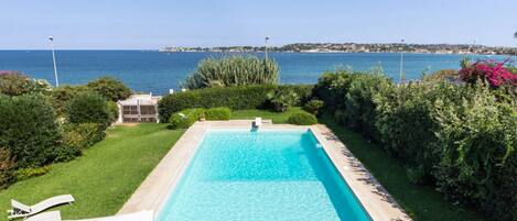 Ein rechteckiger Pool mit klarem, blauem Wasser, umgeben von gepflegter Bepflanzung und Blick auf das Meer.