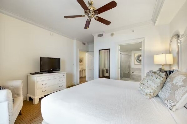 A bedroom with a large bed, a television on a dresser, a ceiling fan, and a mirror.