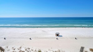 A wide sandy beach with a small structure in the middle, likely a lifeguard station, and a clear blue sky. - 🏖️Beach Front with Great Views - 1BR Sunbird 606W🏖️ (Panama City Beach)
