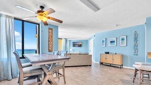 A spacious living room with a wooden dining table, a sofa, and a ceiling fan. - 🏖️Beach Front with Great Views - 1BR Sunbird 606W🏖️ (Panama City Beach)