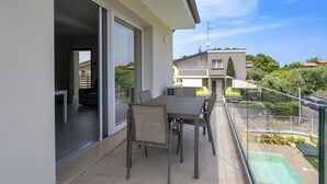 Ein Balkon mit Esstisch und Stühlen, einer Schiebetür aus Glas und Blick auf Nachbarhäuser und Grünflächen.