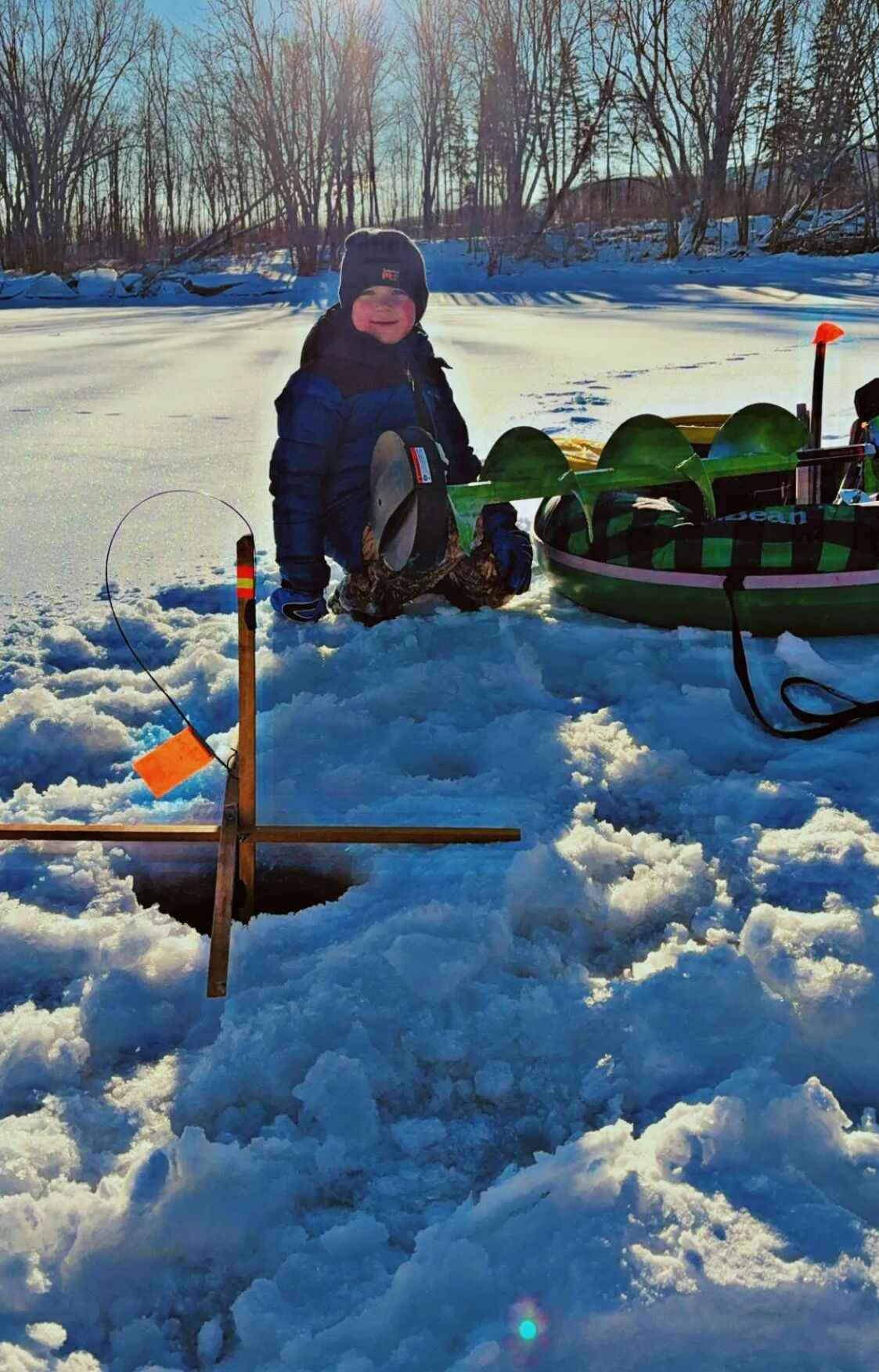 A person in winter clothing near a snow-covered area with a sled and a green inflatable boat.