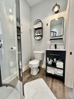 A modern bathroom with a toilet, a black vanity with a mirror, and a glass shower enclosure.