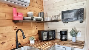 Una cocina compacta con paneles de madera, un lavamanos de acero inoxidable, una cafetera negra y un microondas en la encimera.
