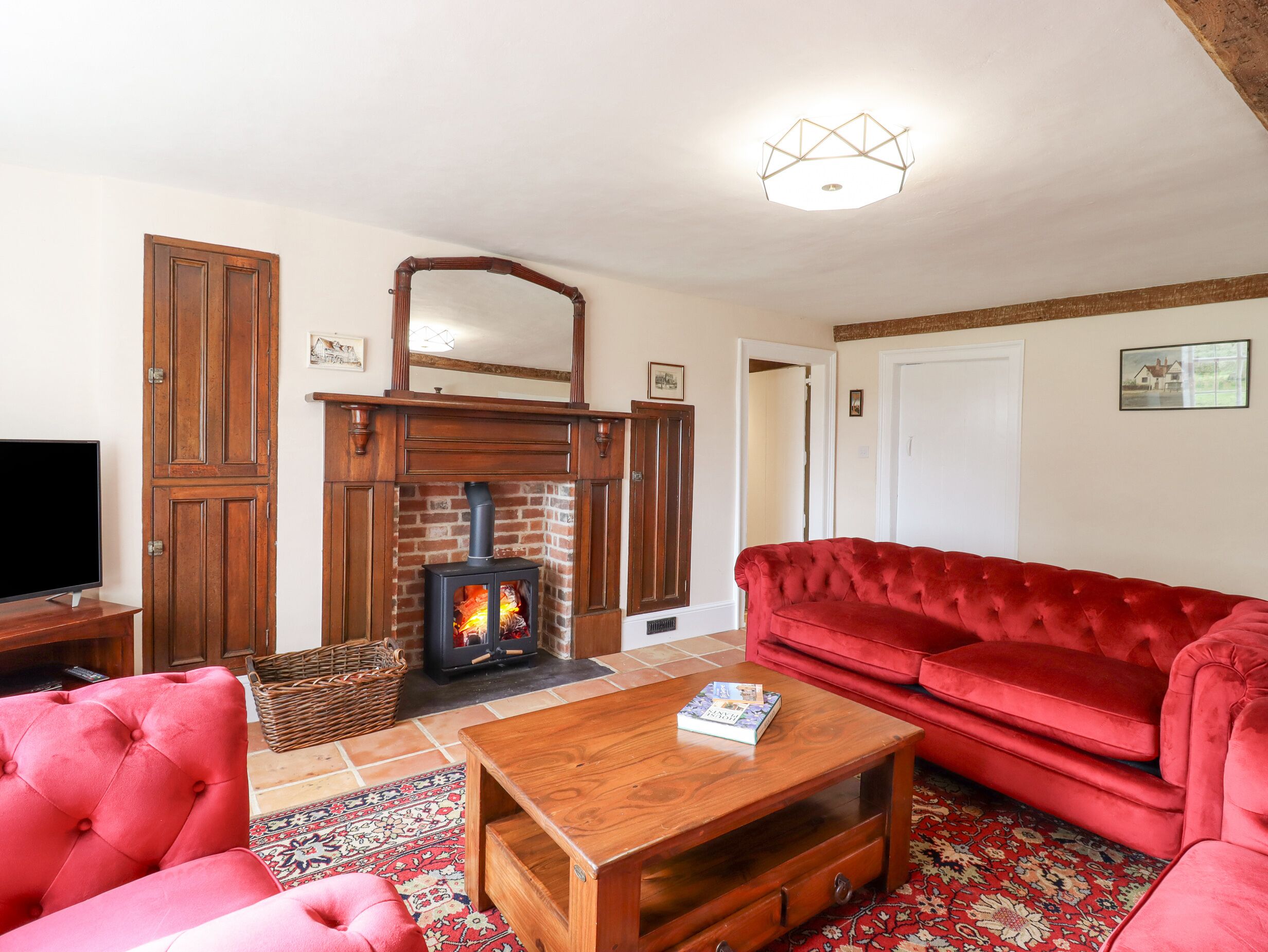 A living room with a brick fireplace, red velvet sofa, wooden coffee table, and a television on a stand.