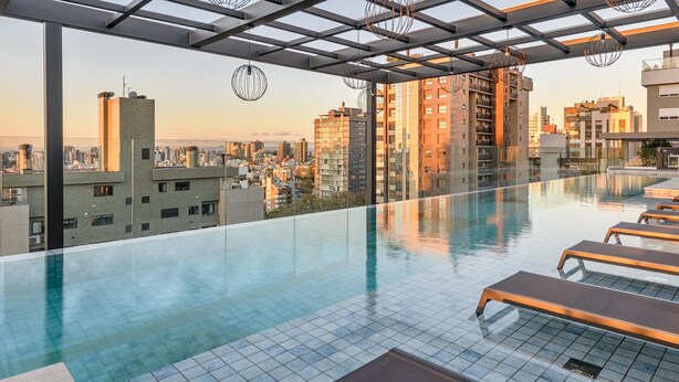 Una piscina infinita en la azotea con sillones, una pérgola y vistas a la ciudad.