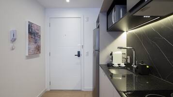 Una cocina compacta con una puerta blanca, un refrigerador, una encimera negra y un teléfono instalado en la pared.