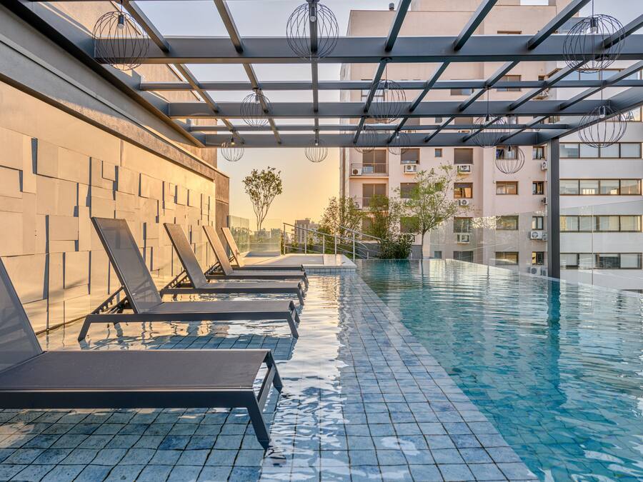 An infinity pool with lounge chairs, a modern architectural design, and a view of surrounding buildings.