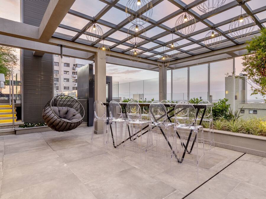 A modern outdoor seating area with a glass table and chairs, a hanging chair, and a view of the cityscape.