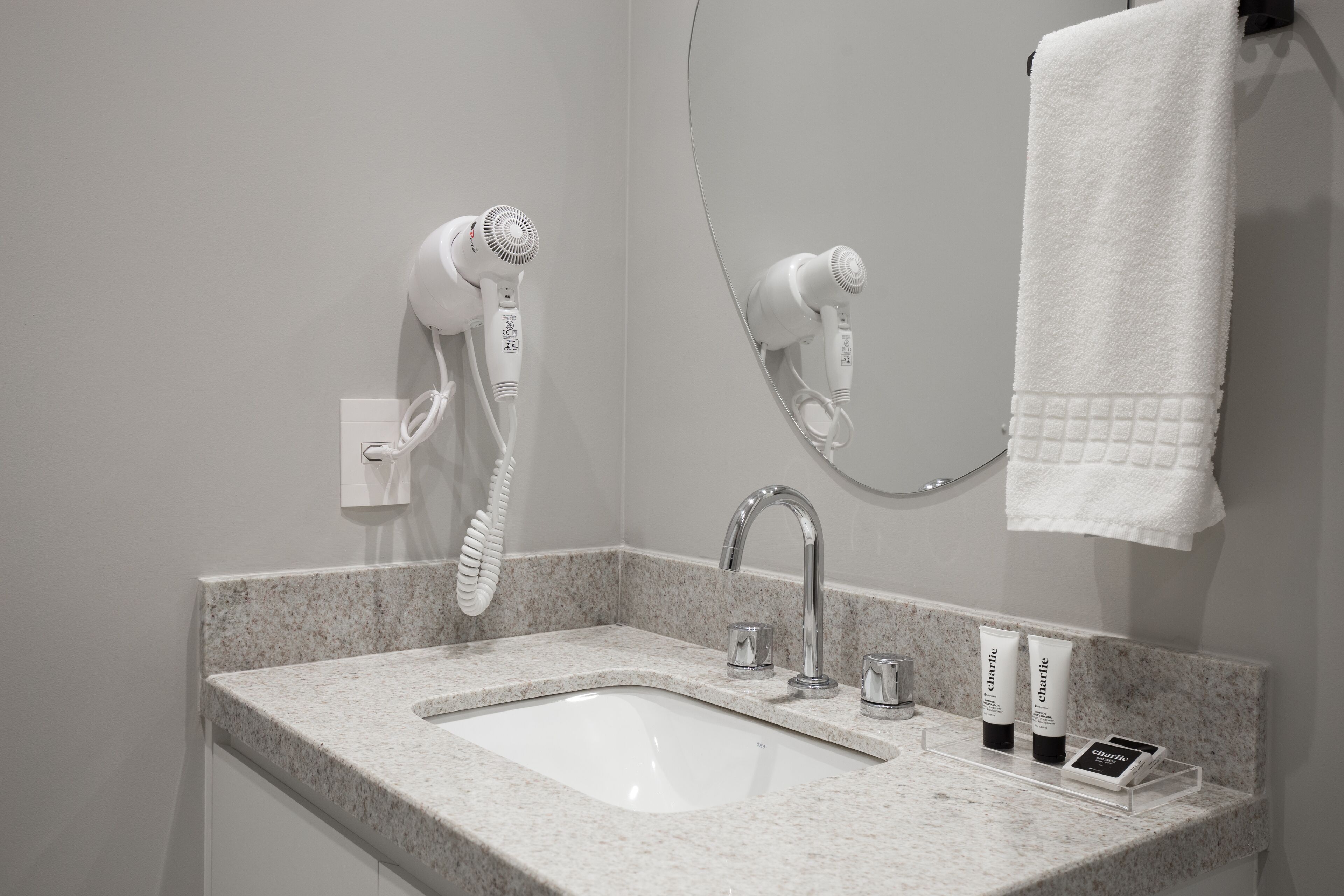 Baño con encimera de granito, lavabo, espejo, toallero y dos secadores de pelo montados en la pared.