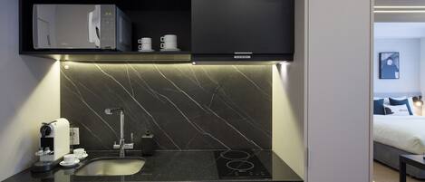 A compact kitchen with a built-in microwave, coffee machine, and a modern sink.