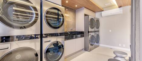 A modern laundry room with four front-loading washing machines, a built-in dryer, and a small seating area with stools.