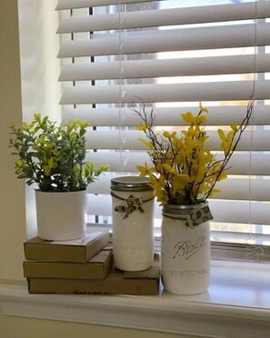Cozy window nook with a potted plant, two Belle Perfection jars, and a stack of books.
